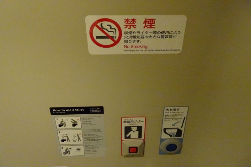 Inside a Shinkansen toilet: a red crew call buzzer (連絡用ブザー) next to the blue flush button (水を流す)